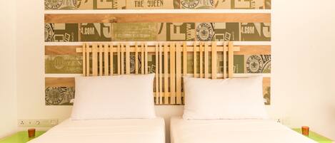 A double bed with white linens, a wooden headboard, and a wall with vintage-style wallpaper.