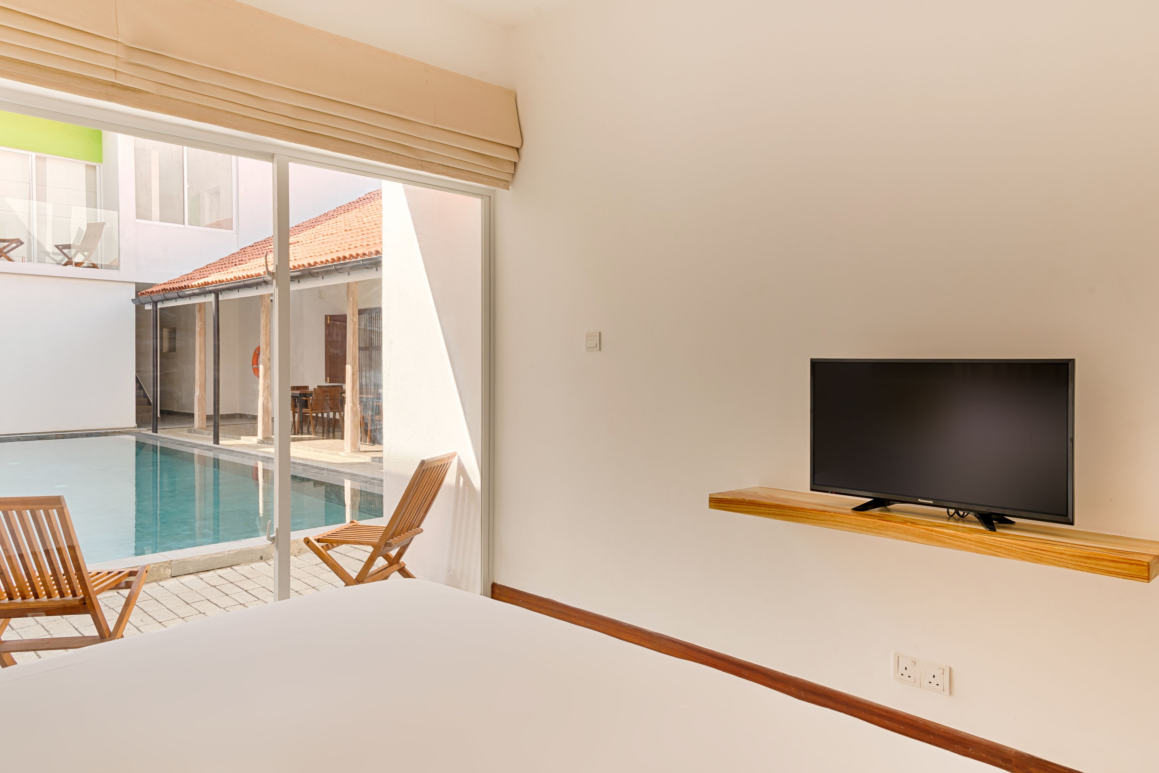 Una camera d'albergo con televisore su uno scaffale di legno, una piscina e due sedie di legno.