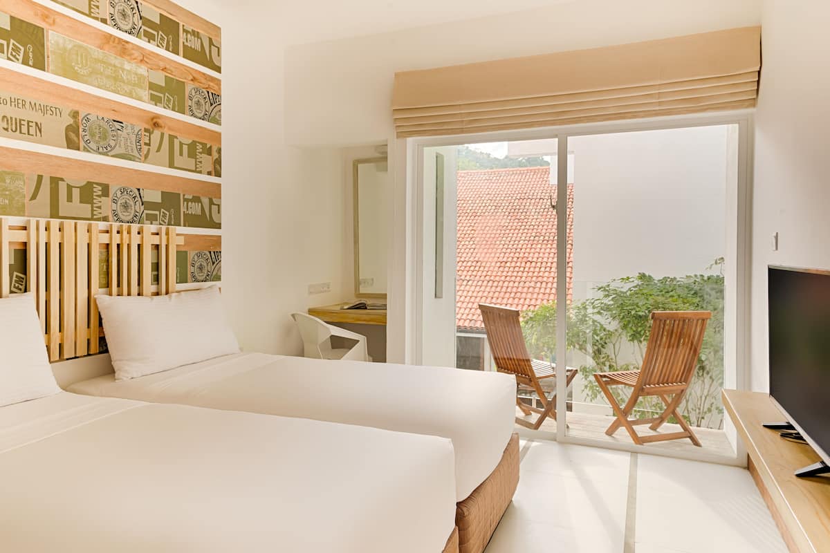 Habitación de hotel moderna con una cama grande, un escritorio y un televisor. Tiene un balcón con sillas y vistas al exterior.