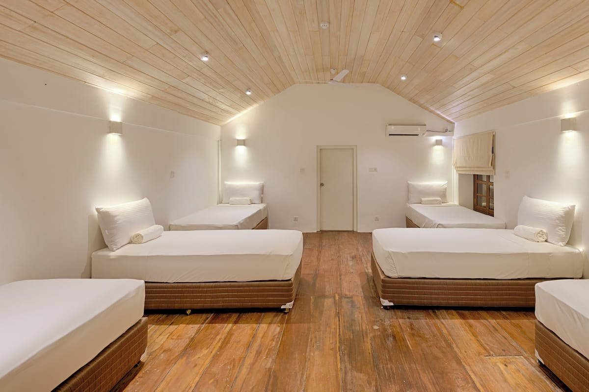 Habitación de hotel con dos camas, piso de madera, paredes blancas y techo inclinado con iluminación empotrada.