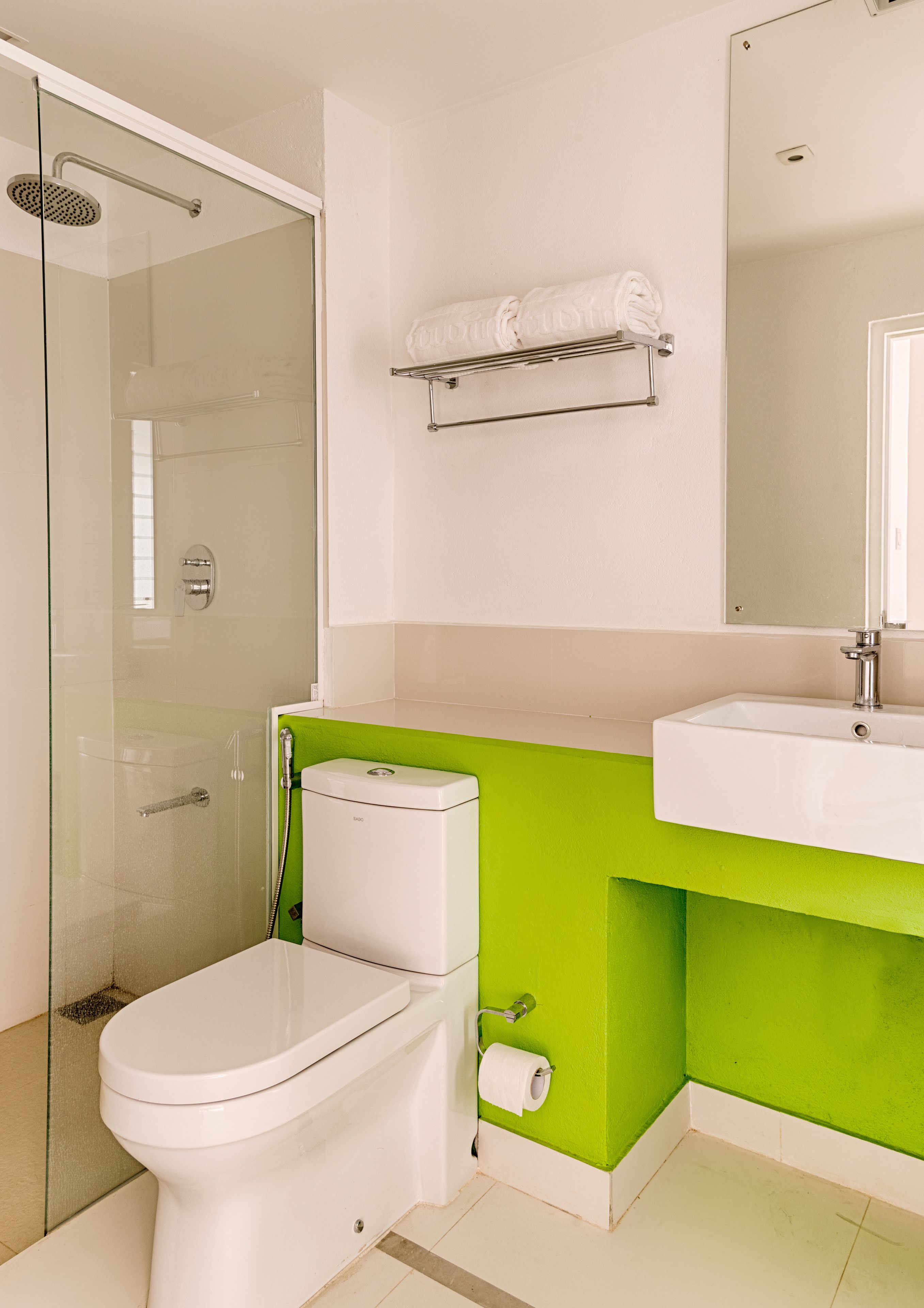 A modern bathroom with a glass-enclosed shower, a white toilet, and a green accent wall.
