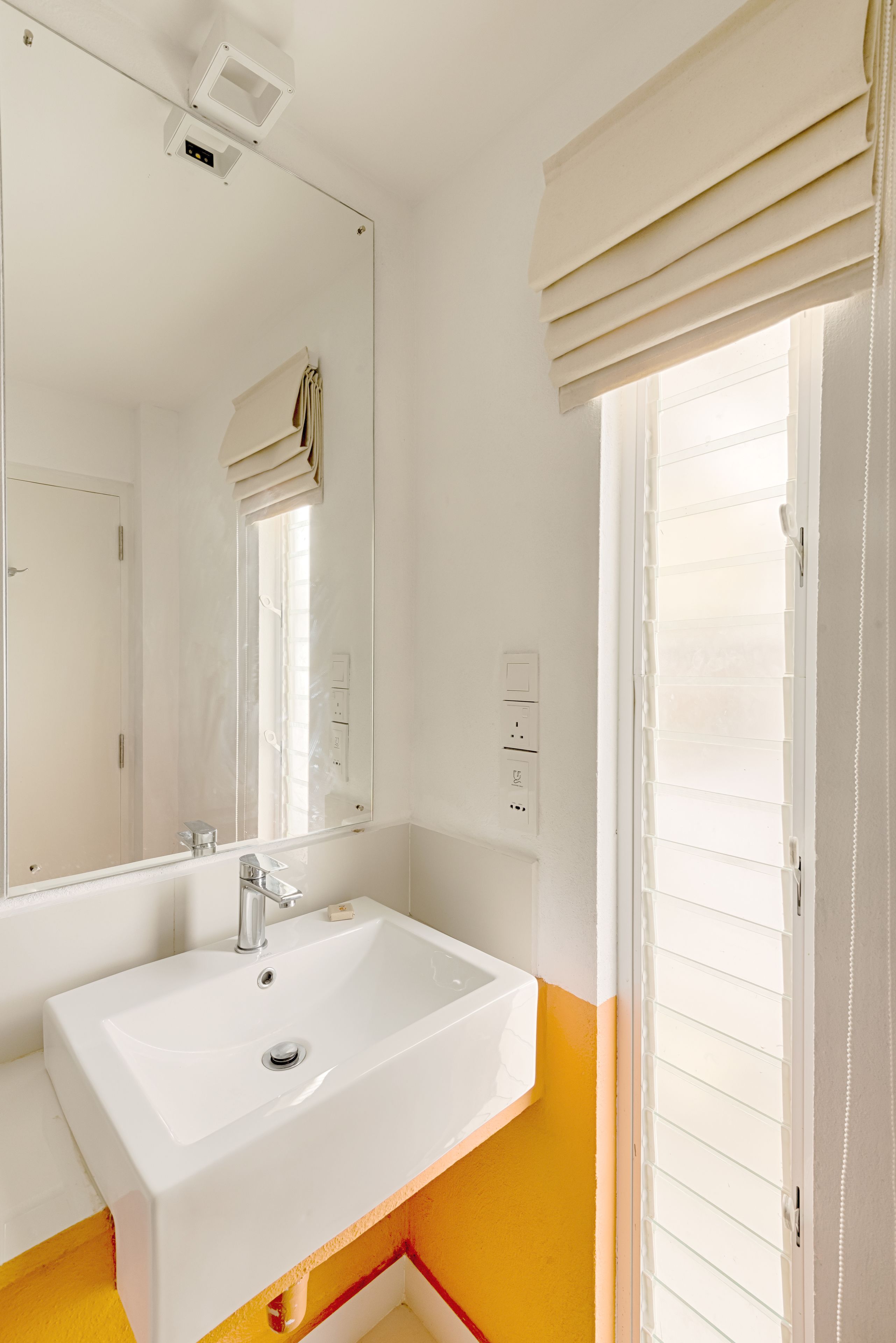 A bathroom with a white sink, mirror, and window with blinds.