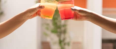 Two hands holding glasses of orange juice in front of a pool.
