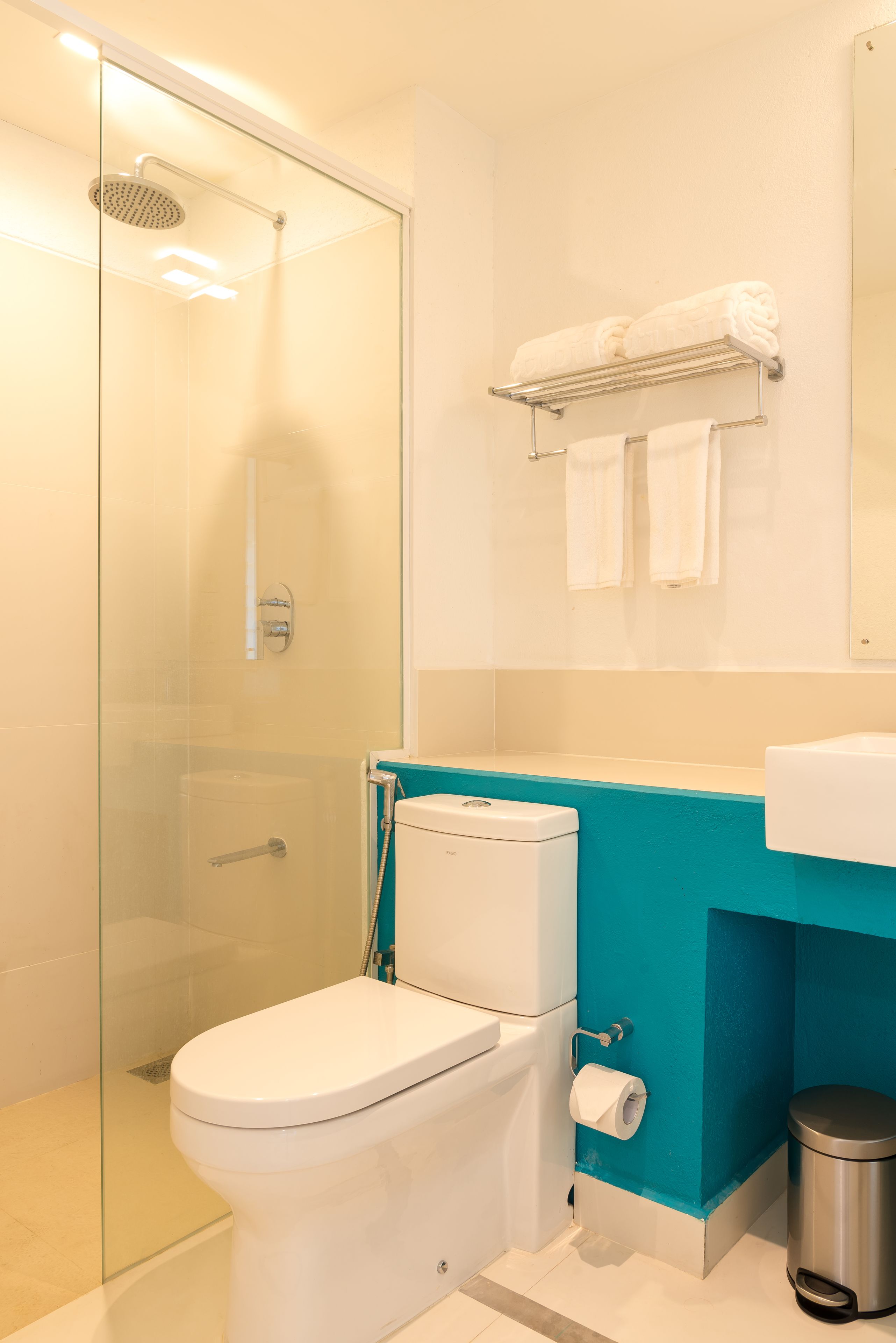Un bagno moderno con doccia in vetro, un WC bianco, una parete decorata in blu e uno scaffale con asciugamani.