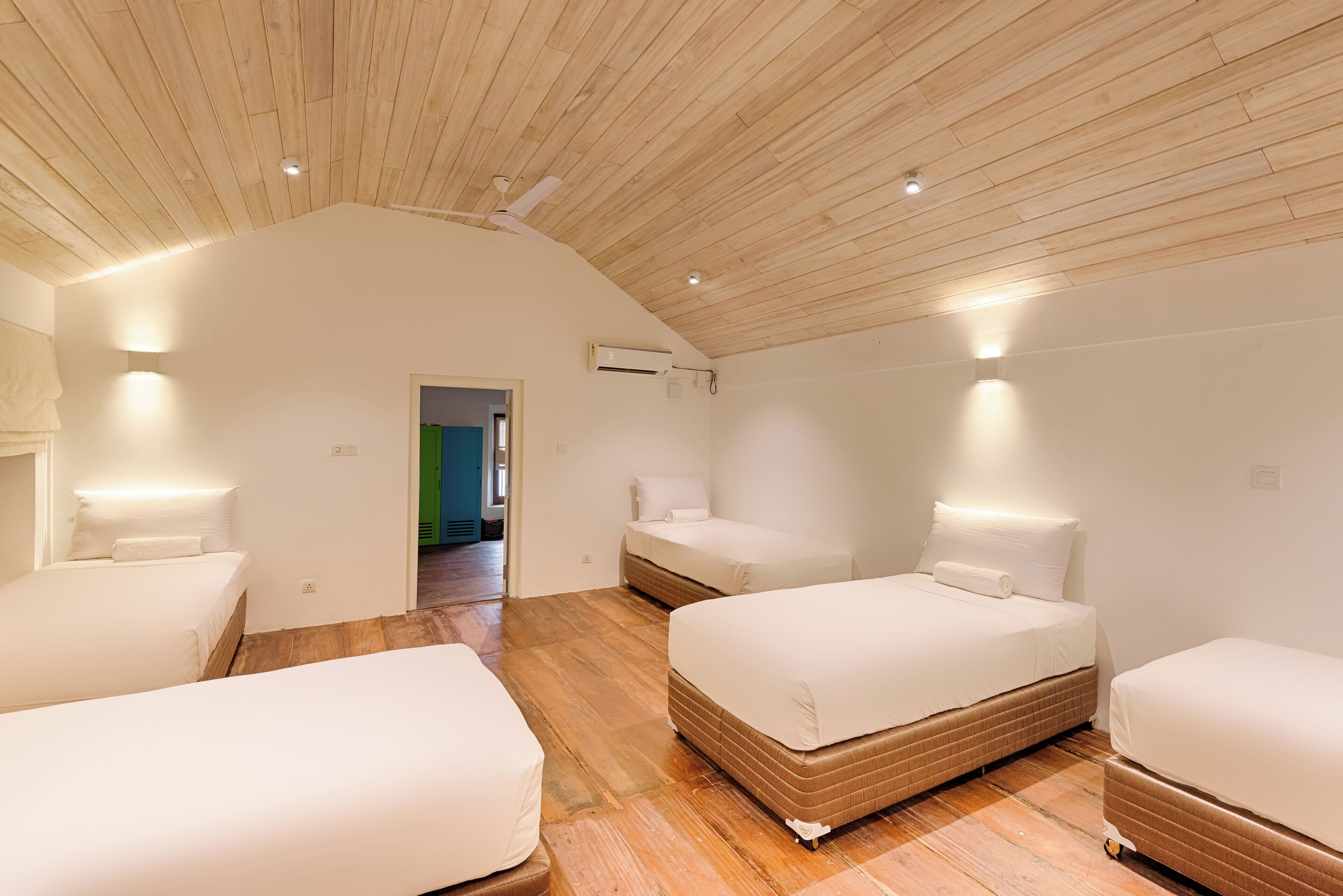 A modern hotel room with a sloped ceiling, wooden flooring, and three beds.