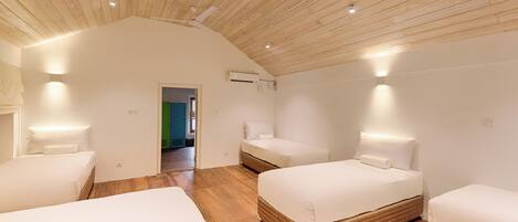 A modern hotel room with a sloped ceiling, wooden flooring, and three beds.
