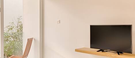 A modern hotel room with a large window, a television on a wooden shelf, and a single bed.