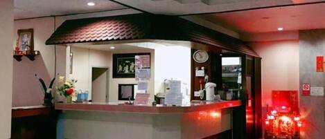 A hotel reception area with a counter, a clock, and a fire alarm.