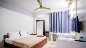 A hotel room with a bed, a desk, a mirror, a television, and a bathroom with a shower curtain. - Pasawang hotel (Hat Yai)