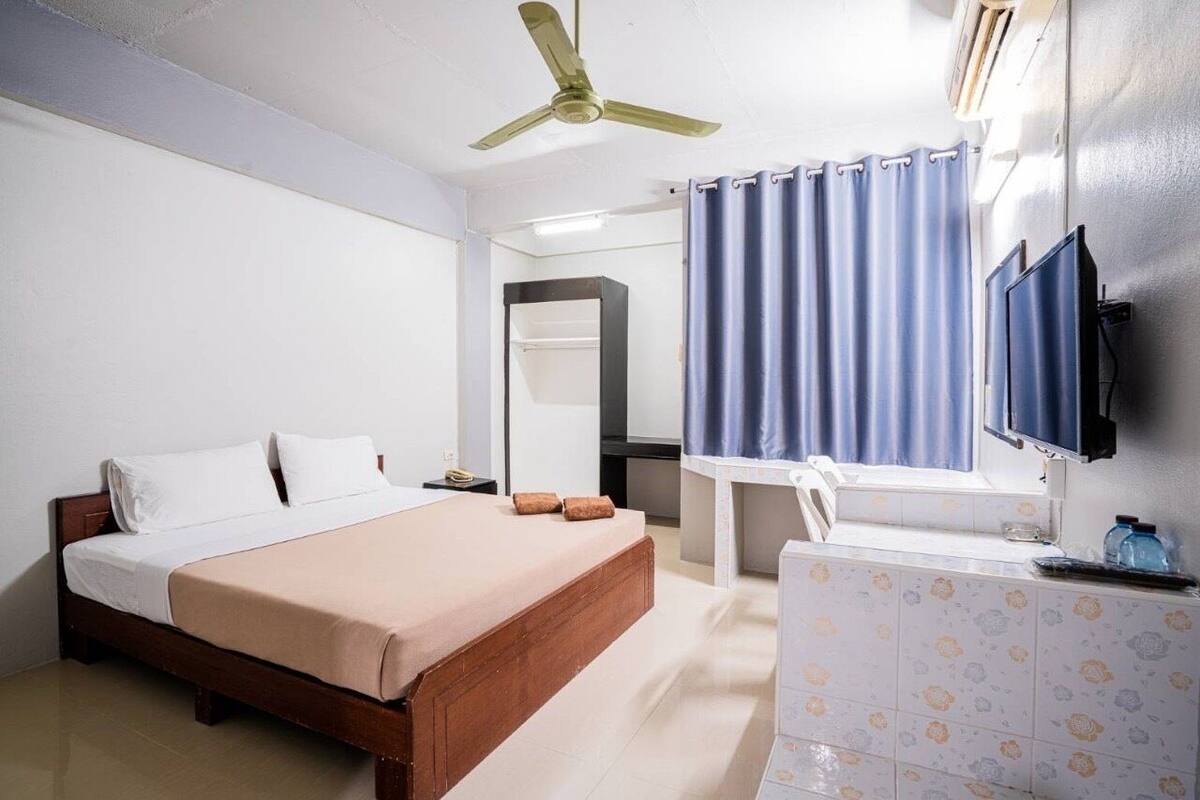 A hotel room with a bed, a desk, a mirror, a television, and a bathroom with a shower curtain.