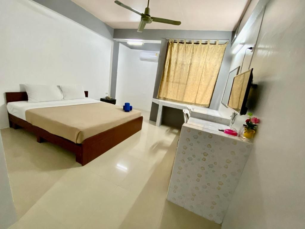 A hotel room with a bed, bedside table, a desk, a chair, a ceiling fan, and a window with curtains.