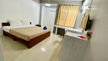 A hotel room with a bed, bedside table, a desk, a chair, a ceiling fan, and a window with curtains.