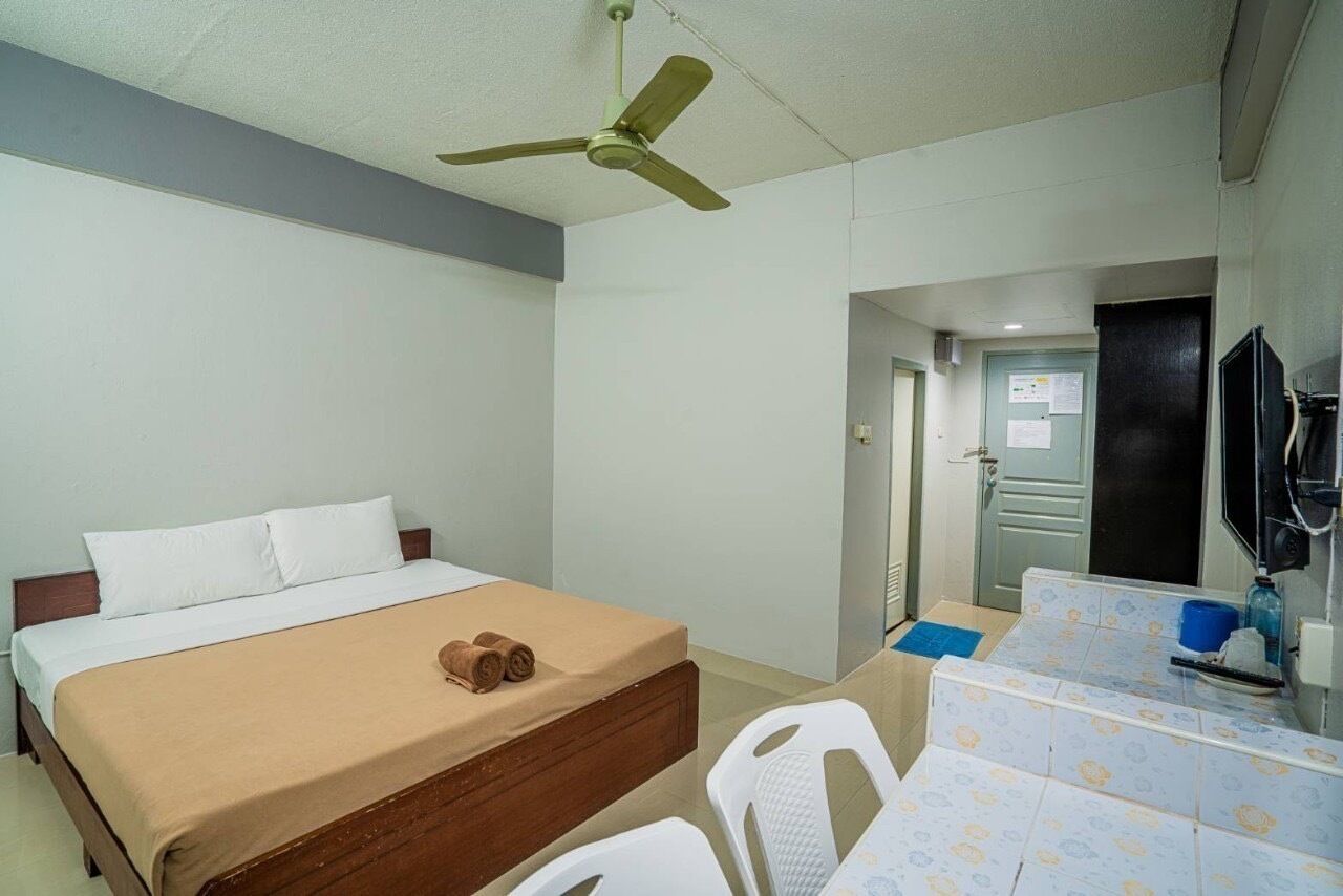 Hotelkamer met een bed, een bureau, een stoel, een plafondventilator en een deur naar een badkamer.
