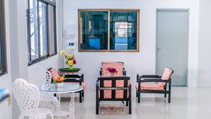 A room with a round glass table surrounded by white chairs and two black chairs with patterned cushions. There is a window with a view of the outside, and a door is visible in the background. - Pasawang hotel (Hat Yai)