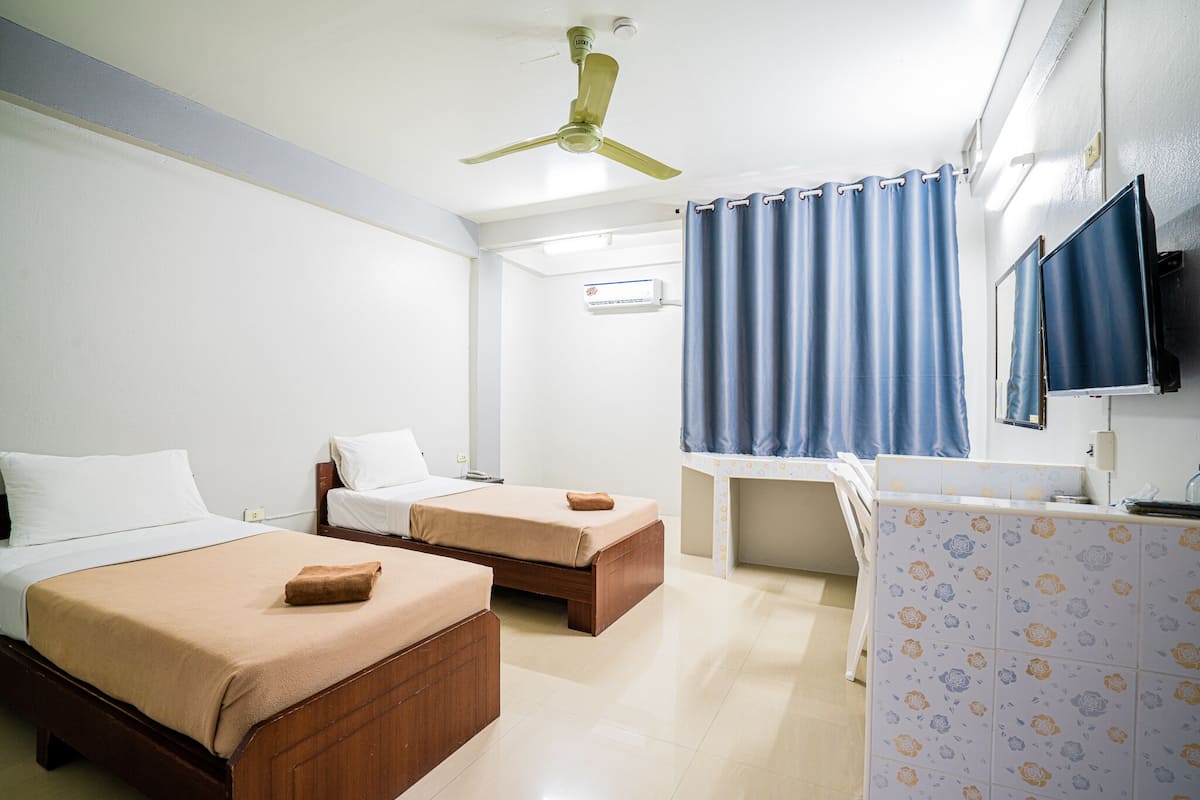 A hotel room with two beds, a desk, a bathroom, and a ceiling fan.