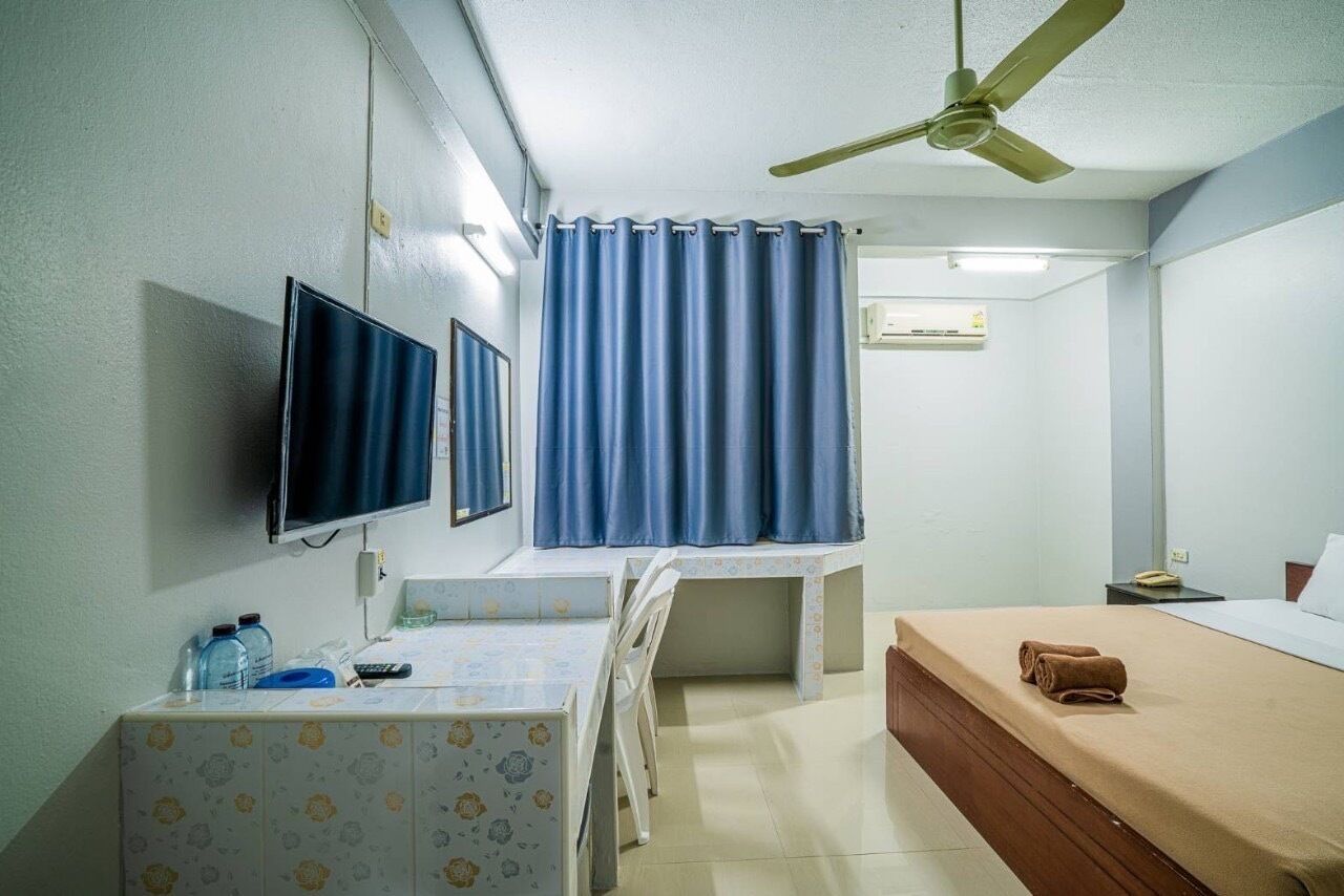 A hotel room with a bed, a desk with a chair, a television, and a ceiling fan.
