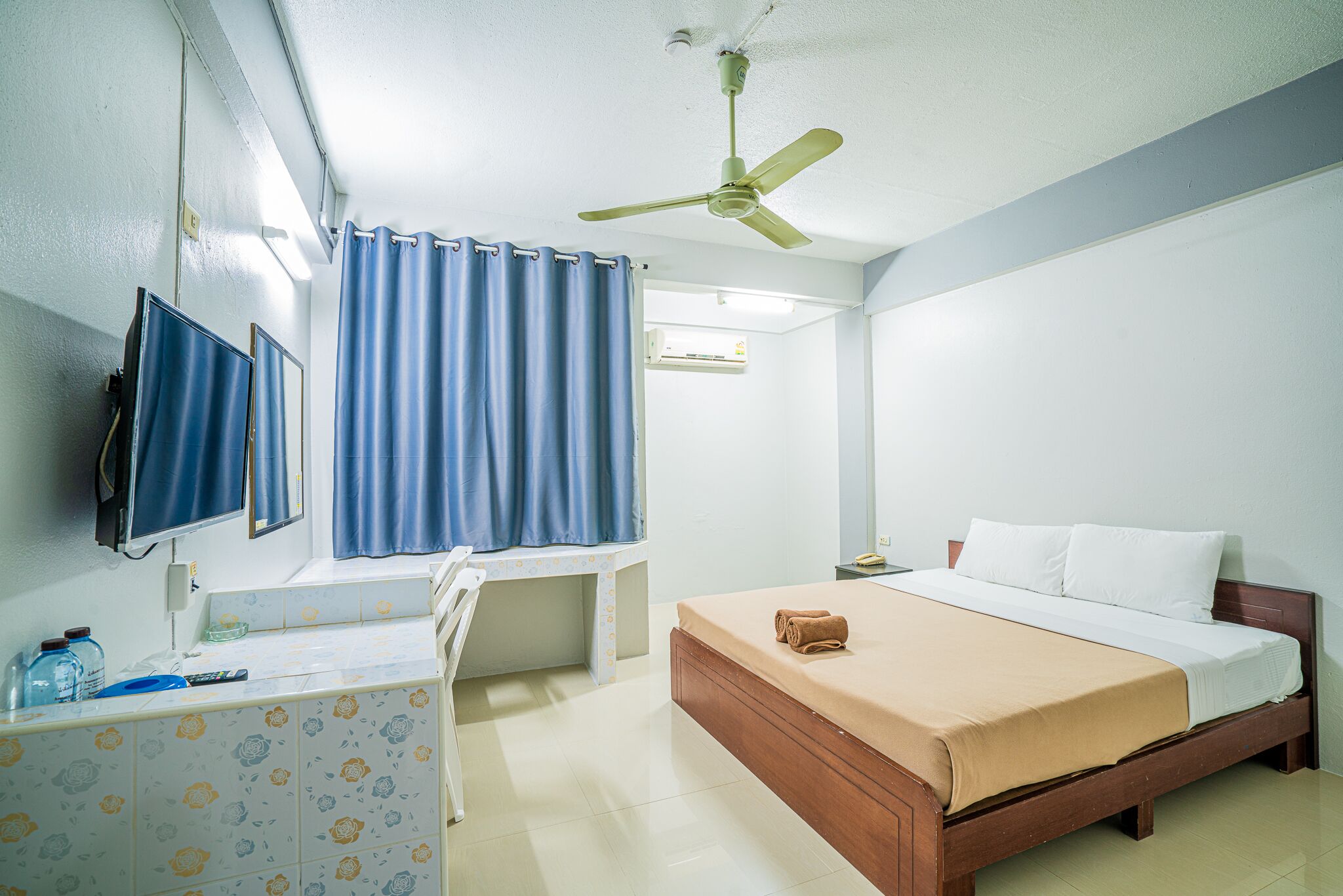 A hotel room with a bed, a desk, a television, and a ceiling fan.