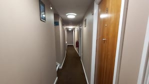 A narrow, carpeted hallway with a wooden door on the right and a framed picture on the left wall.