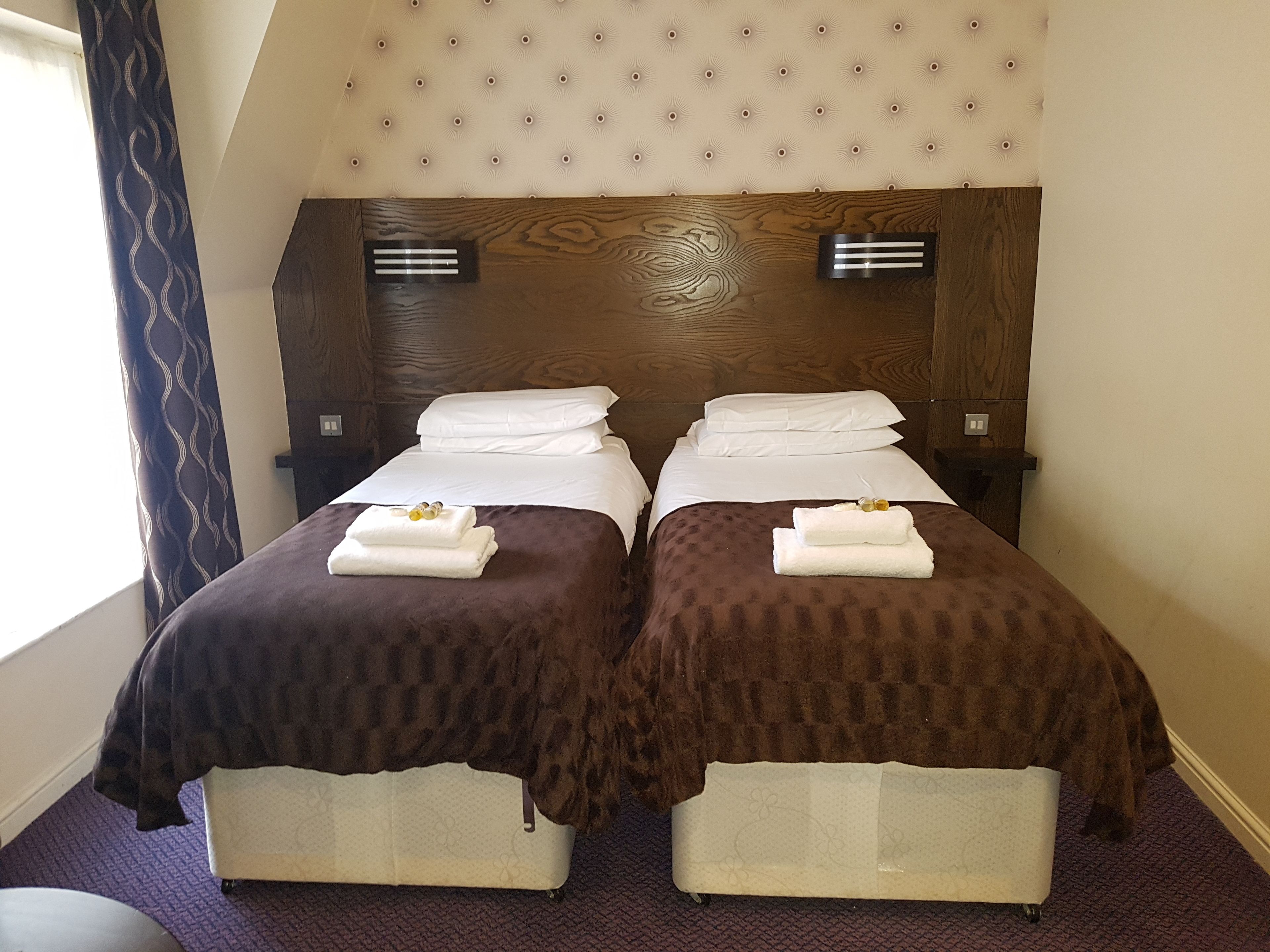 A double room with two beds, each with a brown bedspread and white pillows, and a headboard with a tufted design.