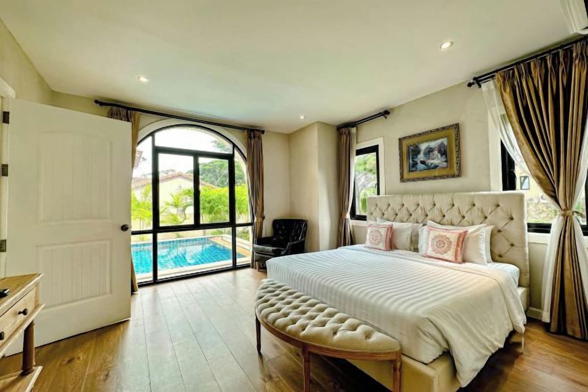 A bedroom with a large bed, a view of a swimming pool, and a door leading outside.