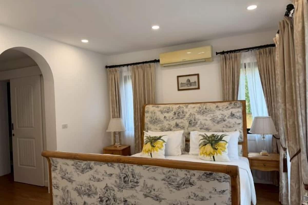 A bedroom with a bed, two nightstands, a wall-mounted air conditioner, and a door.