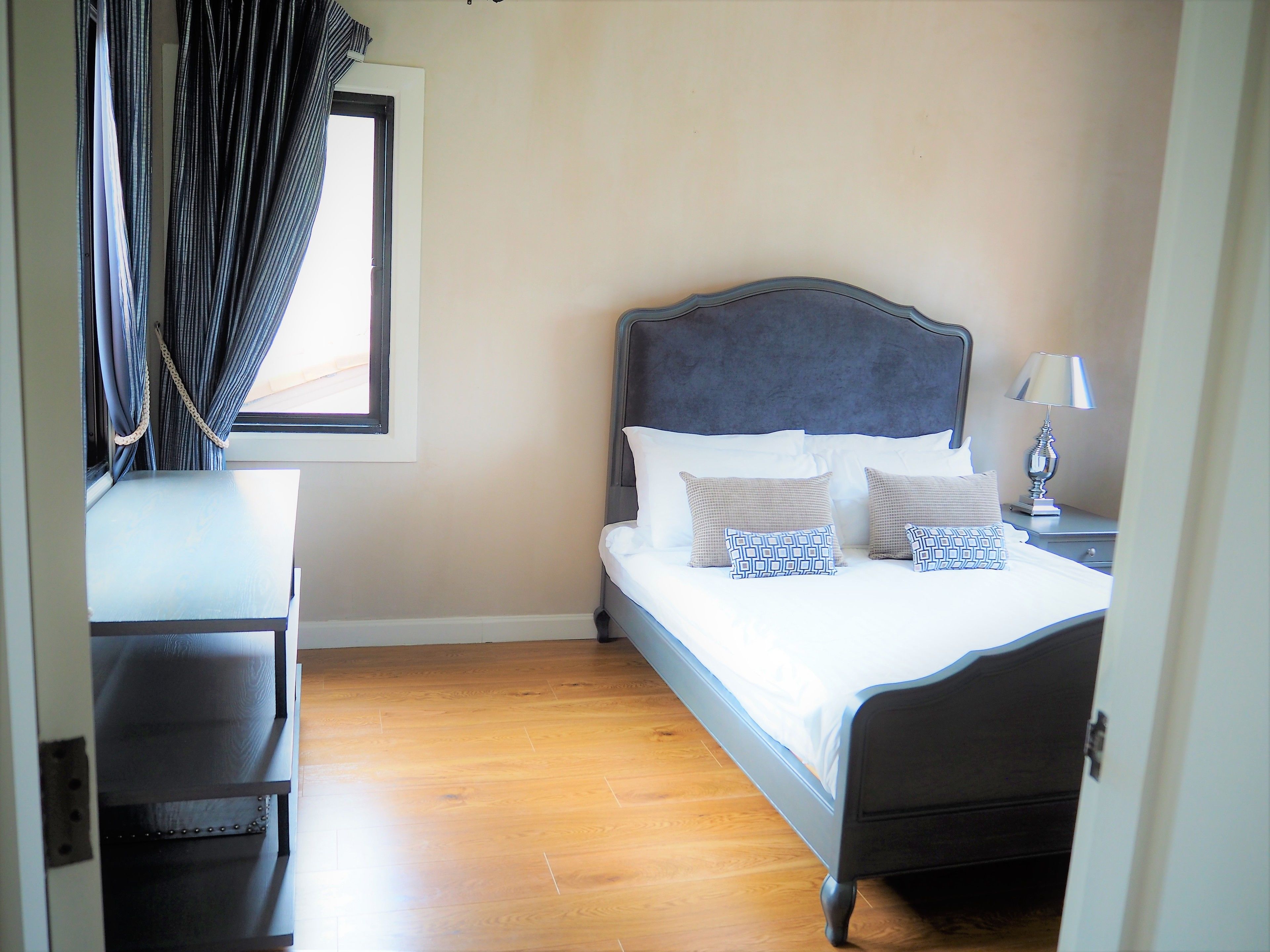 A neatly made bed with patterned pillows, a bedside lamp, and a window with curtains.