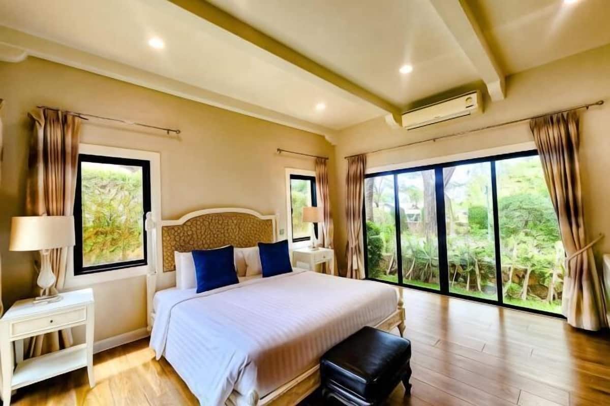 A bedroom with a large bed, two bedside tables, a bench, and a view through large windows.