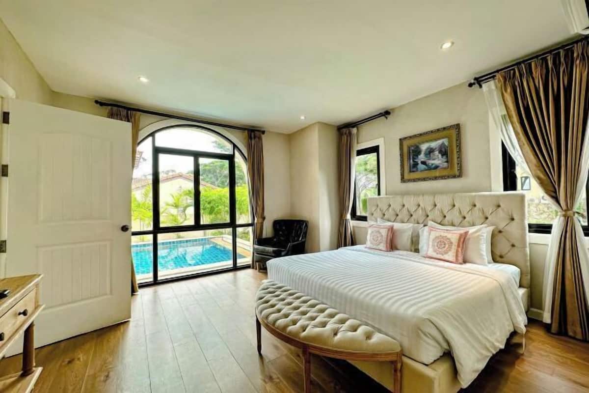 A bedroom with a large bed, a bench, a door leading to a pool, and a framed picture on the wall.