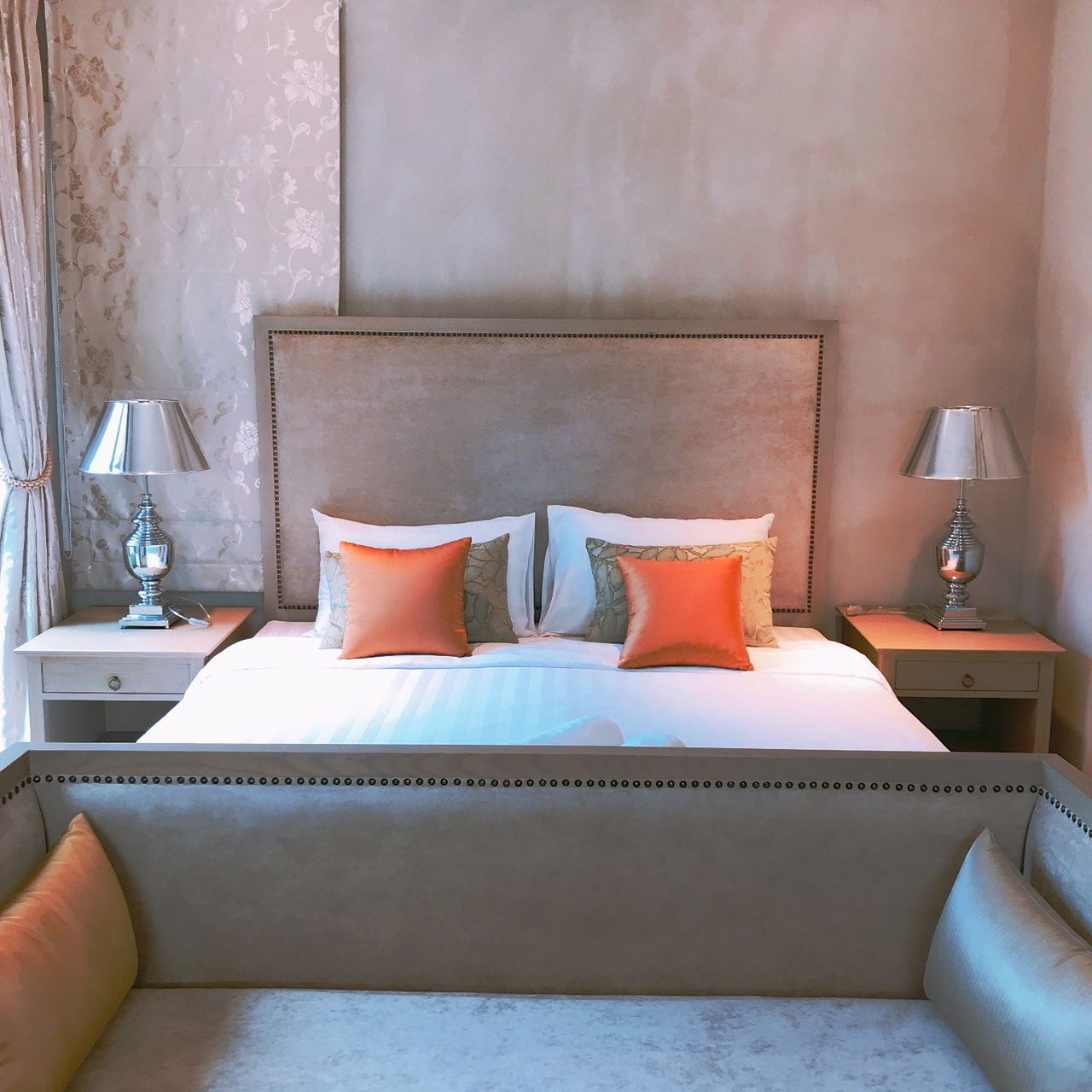 A neatly made bed with two pillows, a headboard, and two bedside tables with lamps.