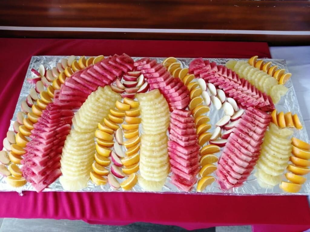 En bakke med skåret frugt arrangeret i et dekorativt mønster på et bord dækket af et rødt stof.