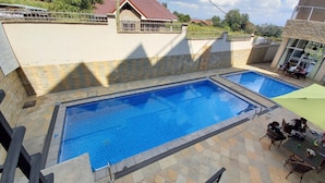 A swimming pool with a tiled deck and a covered seating area.