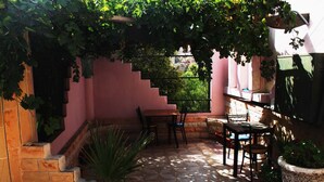 A patio with a stone floor, a table and chairs, a potted plant, and a staircase leading to an upper level. - Cairwan Hotel (Al-Karak)