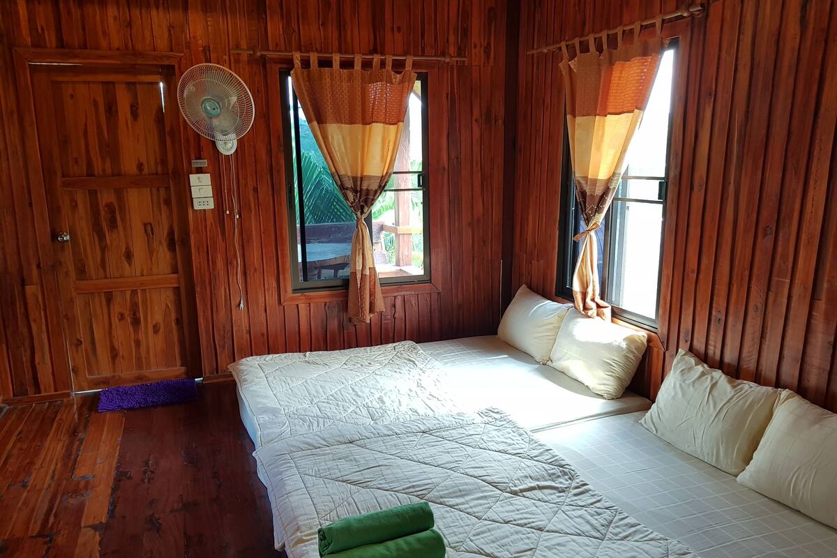 Una habitación de madera con cama, cortinas y un ventilador.