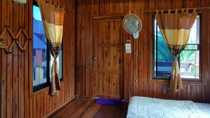 A wooden room with a bed, a fan, and two windows with curtains. - Baan Phanawan Resort (Khao Kho)
