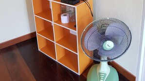 A television on a wooden stand, a mirror on the wall, and a standing fan. - Baan Phanawan Resort (Khao Kho)