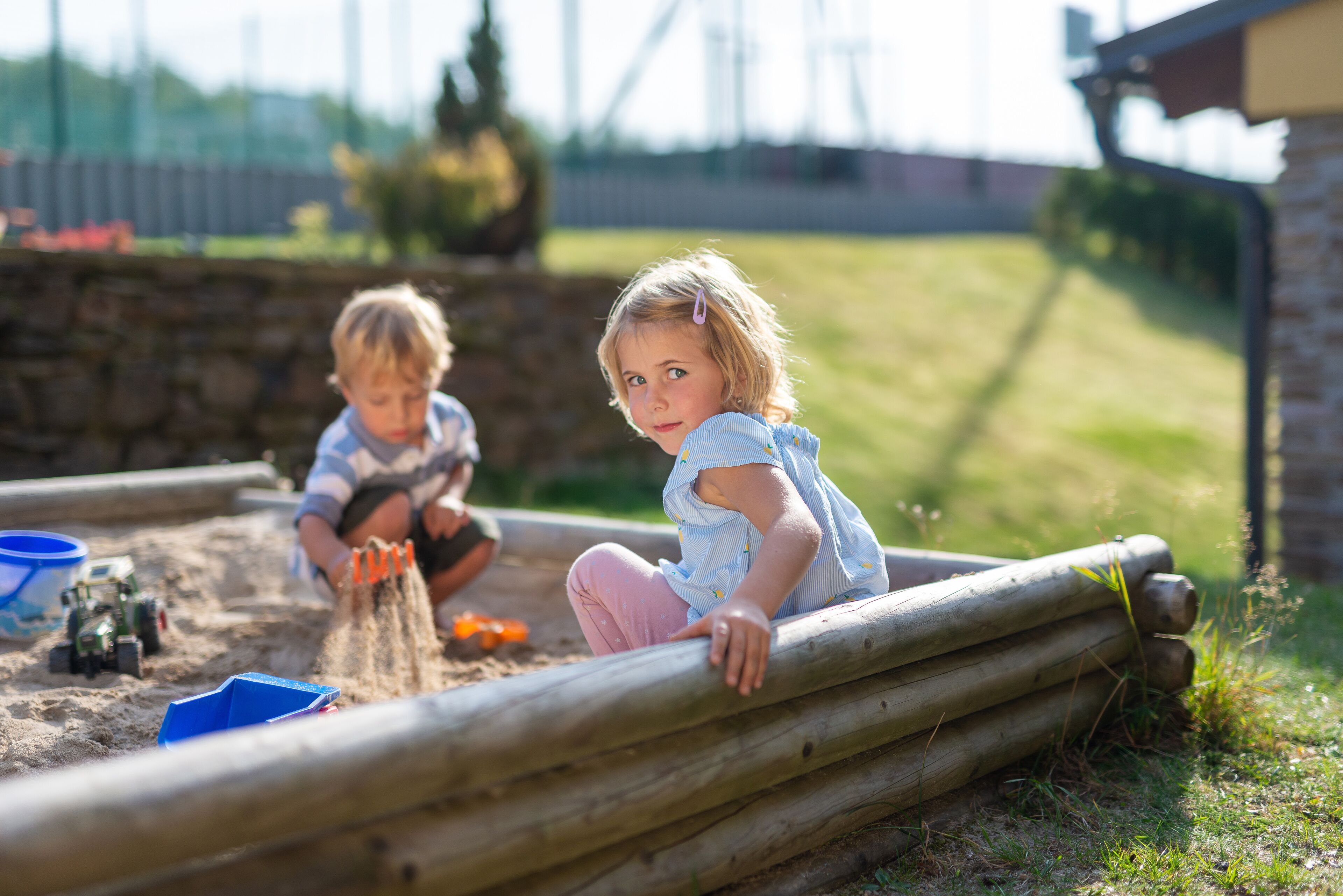 Two children playing in a sandbox with toys and a blue container.