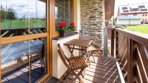 A wooden deck with a table and chairs, a stone wall, and a window with a view of the surrounding area. - Apartmany Engadin (Bozi Dar)