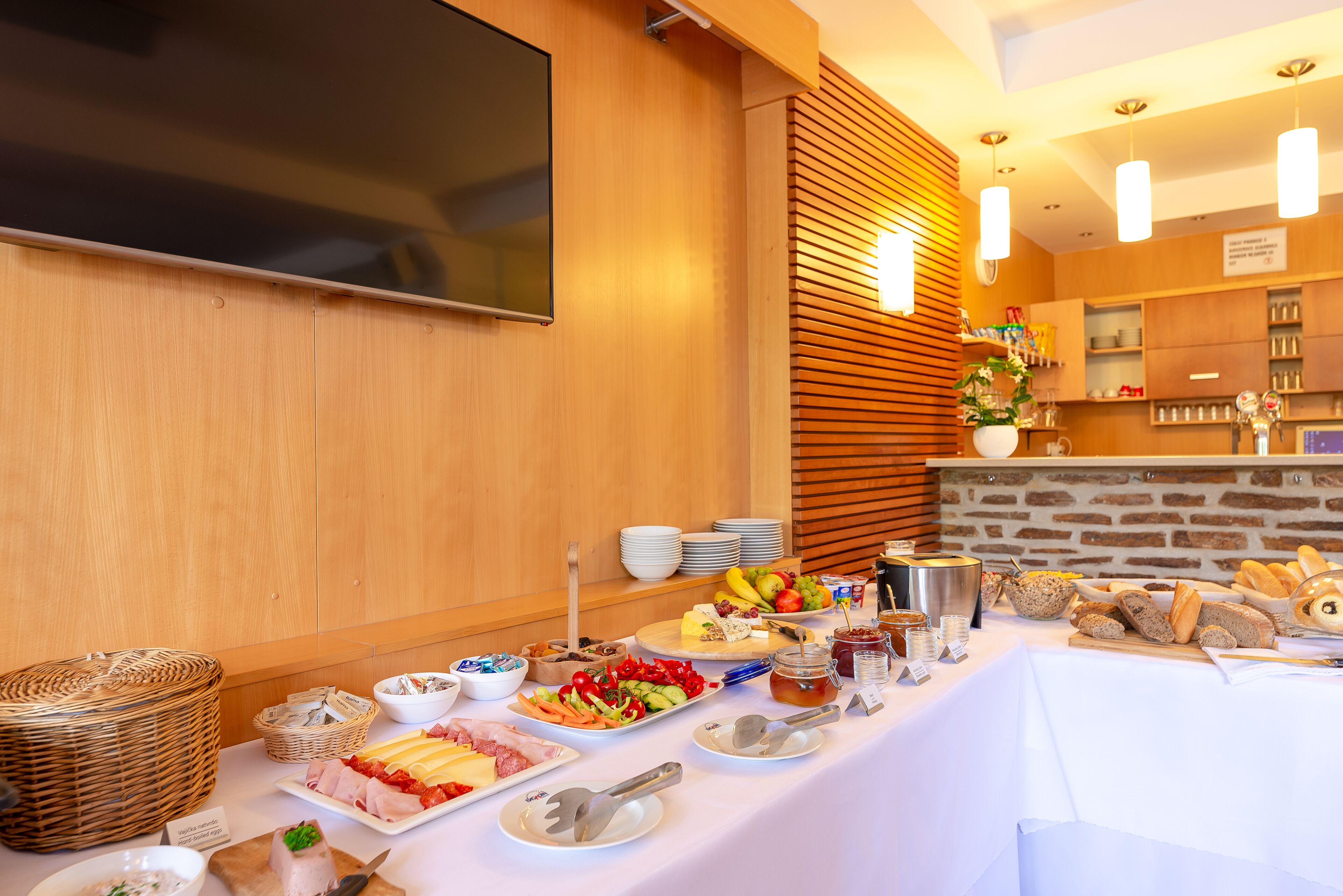Ein reichhaltiges Buffet mit verschiedenen Speisen, ein an der Wand befestigter Fernseher und eine Backsteinwand im Hintergrund.