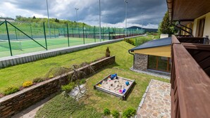 A tennis court with a net, a small play area with sand and toys, and a stone wall. - Apartmany Engadin (Bozi Dar)