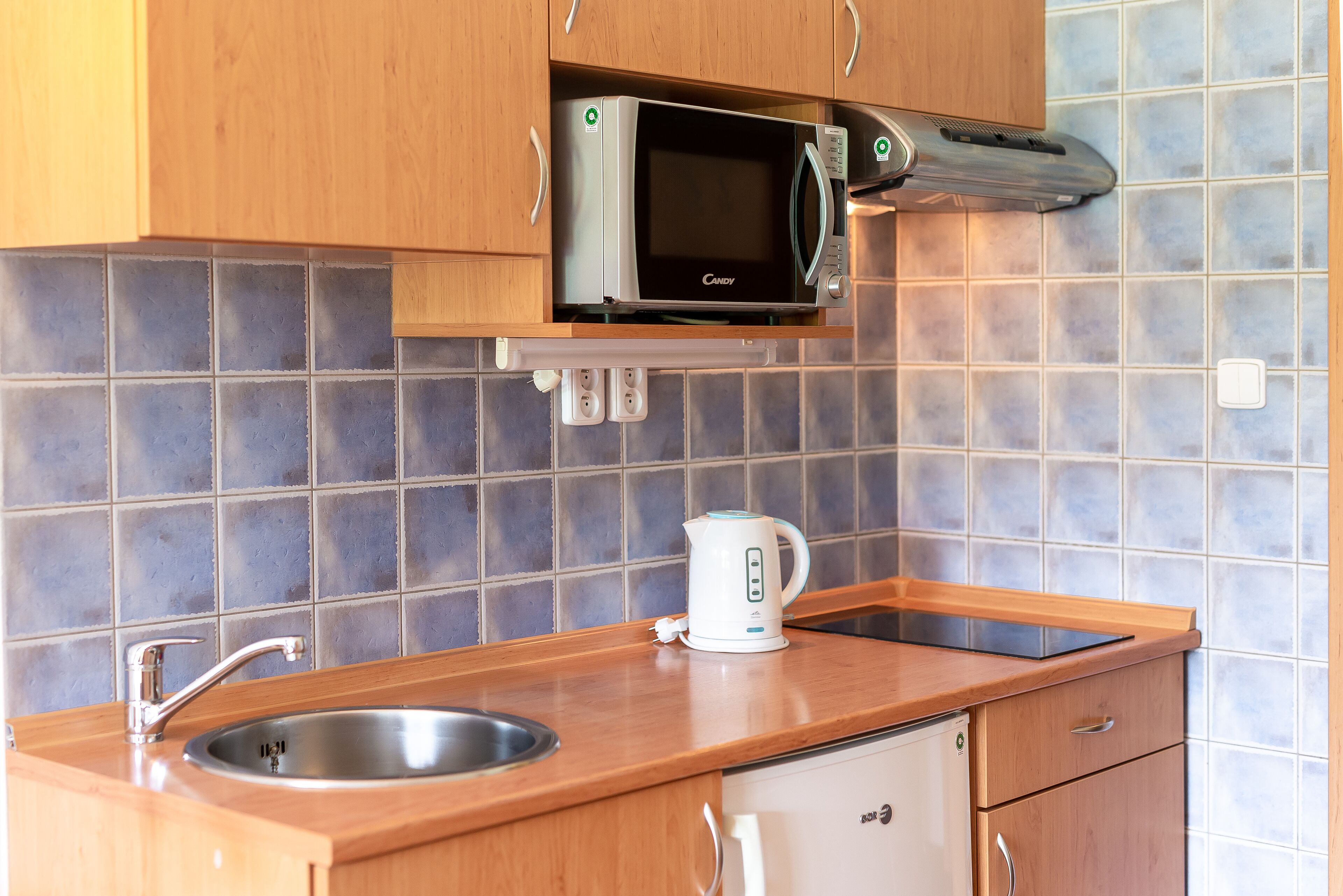 A kitchen with a microwave, kettle, sink, and wooden cabinets.