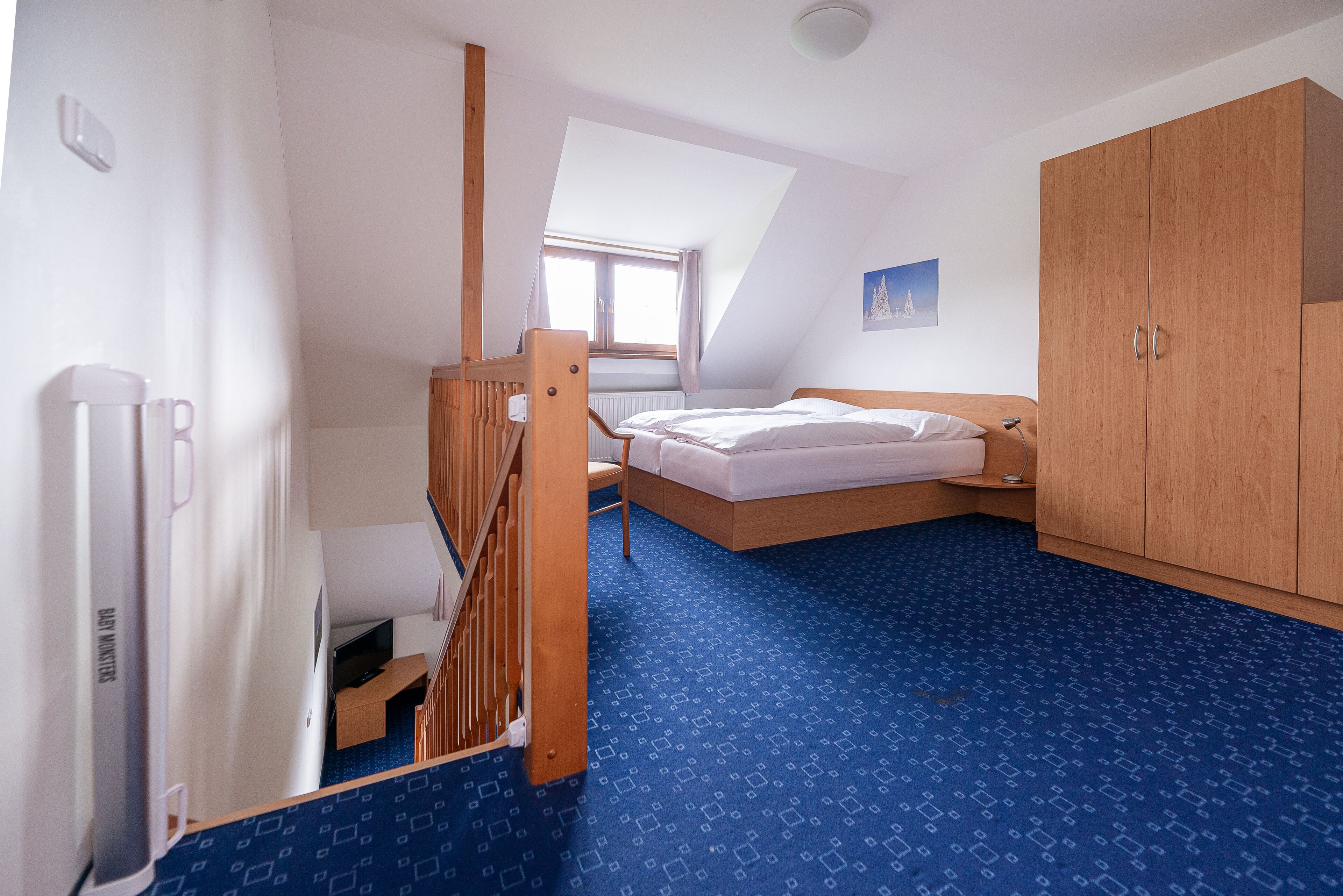 A bedroom with a sloped ceiling, a bed, a wardrobe, and a radiator.