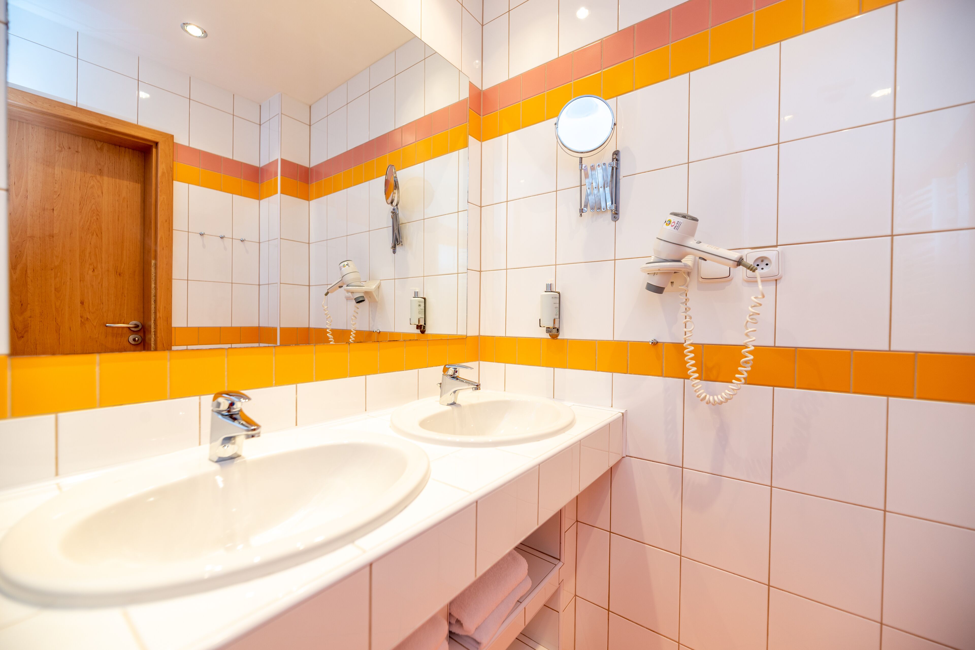 A bathroom with two sinks, a mirror, a hairdryer, and a towel rack.