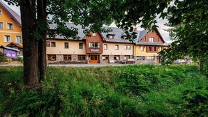 A row of traditional European-style buildings with a central entrance, surrounded by lush greenery. - Apartmany Engadin (Bozi Dar)