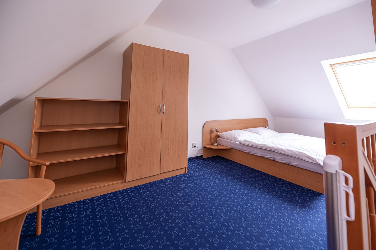 Una habitación pequeña con una cama individual, un armario de madera, un escritorio y una silla.