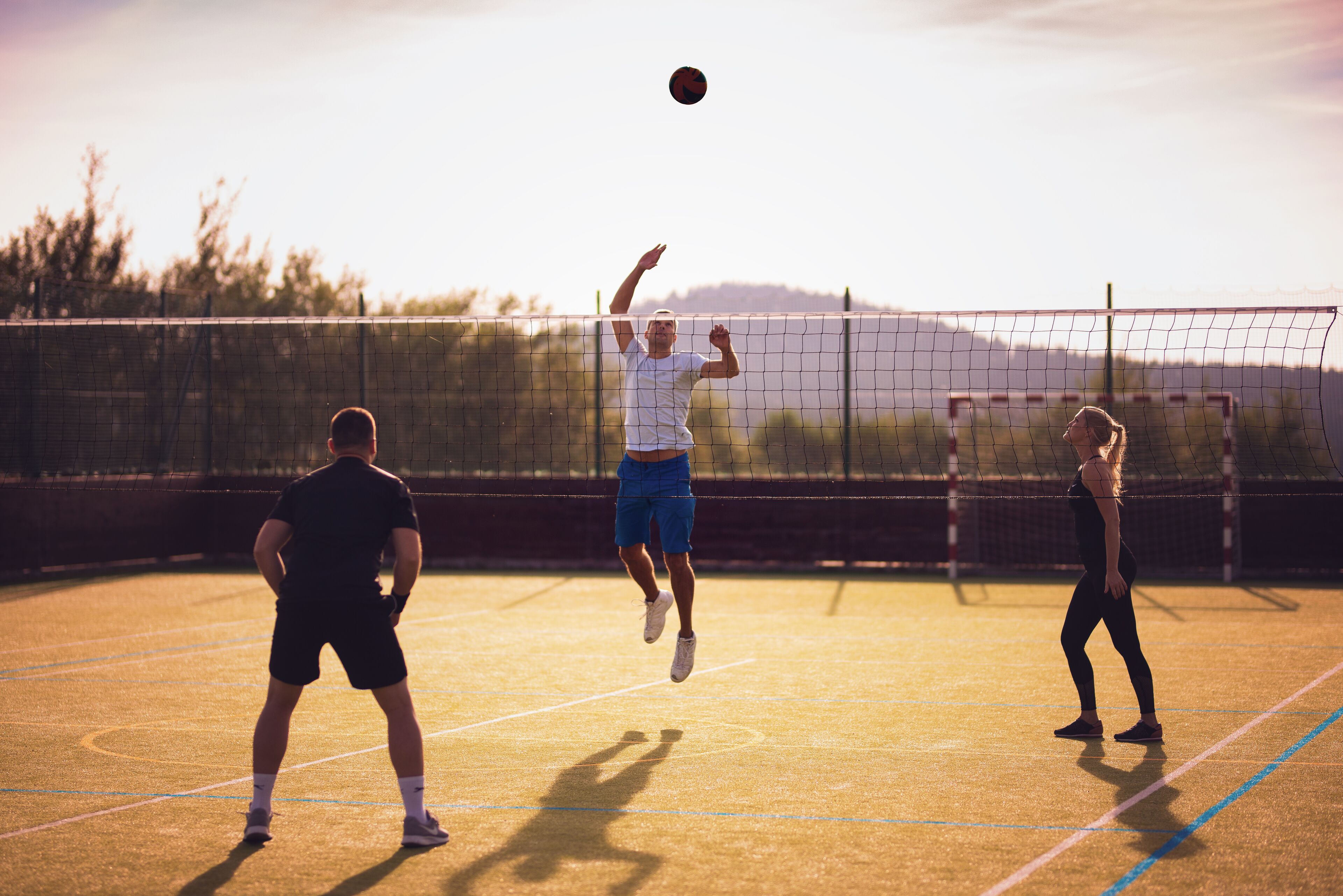 A tennis court with players in motion, a net, and a clear sky.