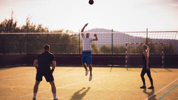 A tennis court with players in motion, a net, and a clear sky.