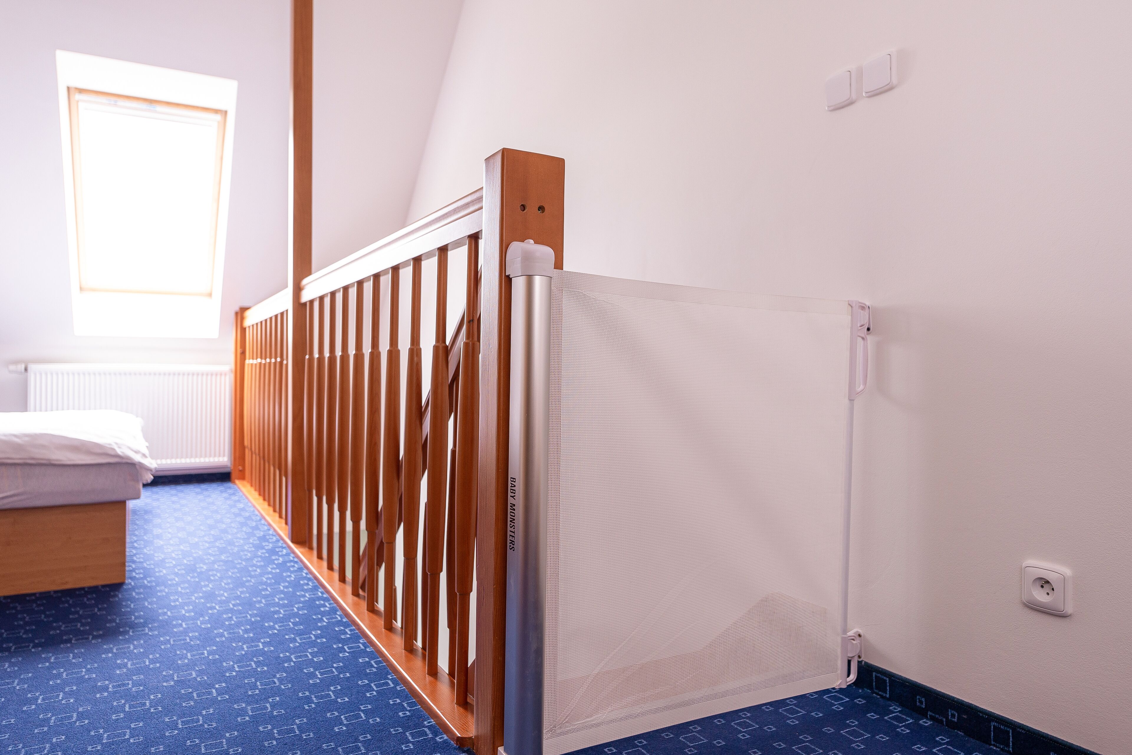 A room with a bed, a window, a radiator, and a wooden railing.