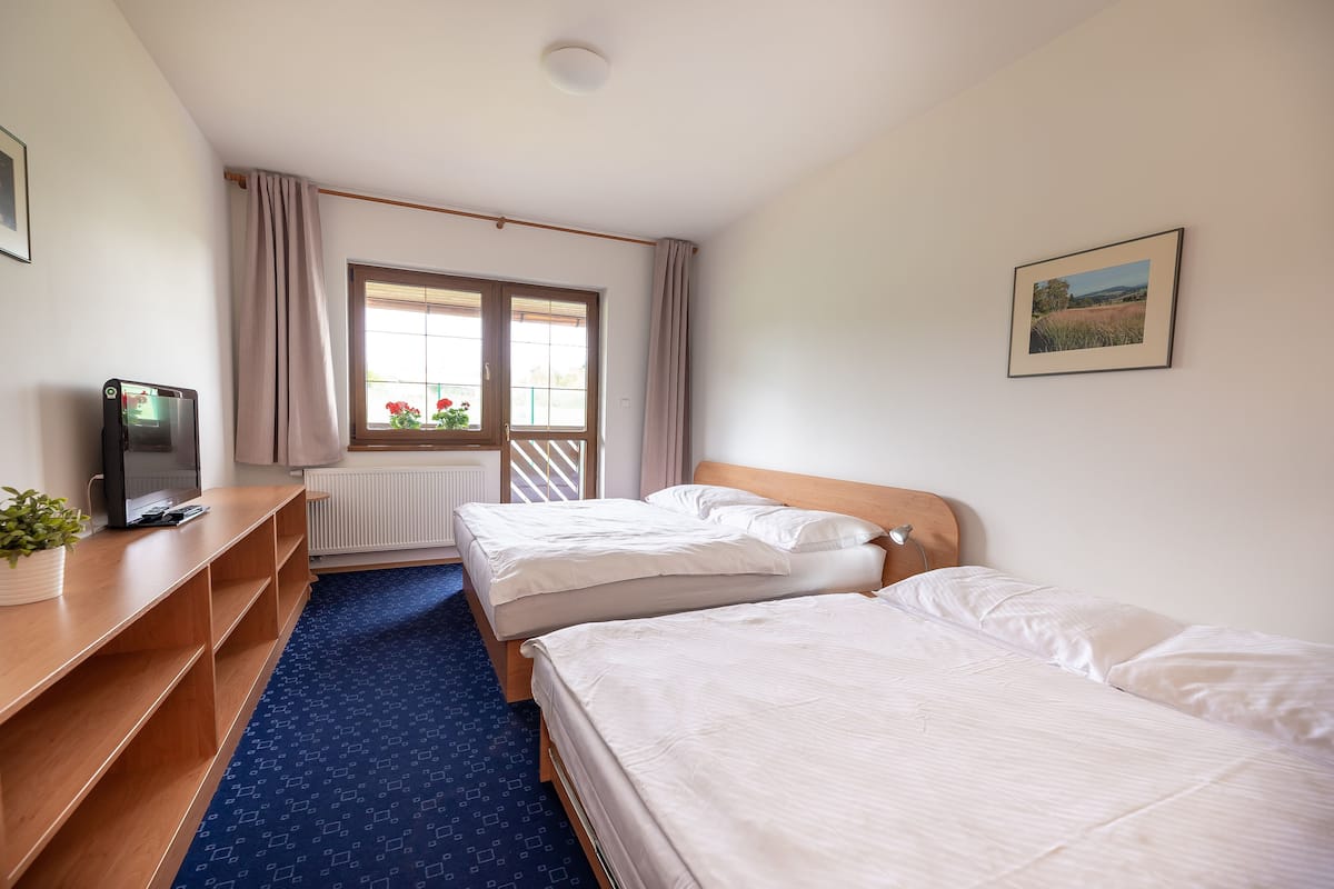 Habitación de hotel con dos camas, un escritorio con computadora, una ventana con cortinas y un cuadro en la pared.