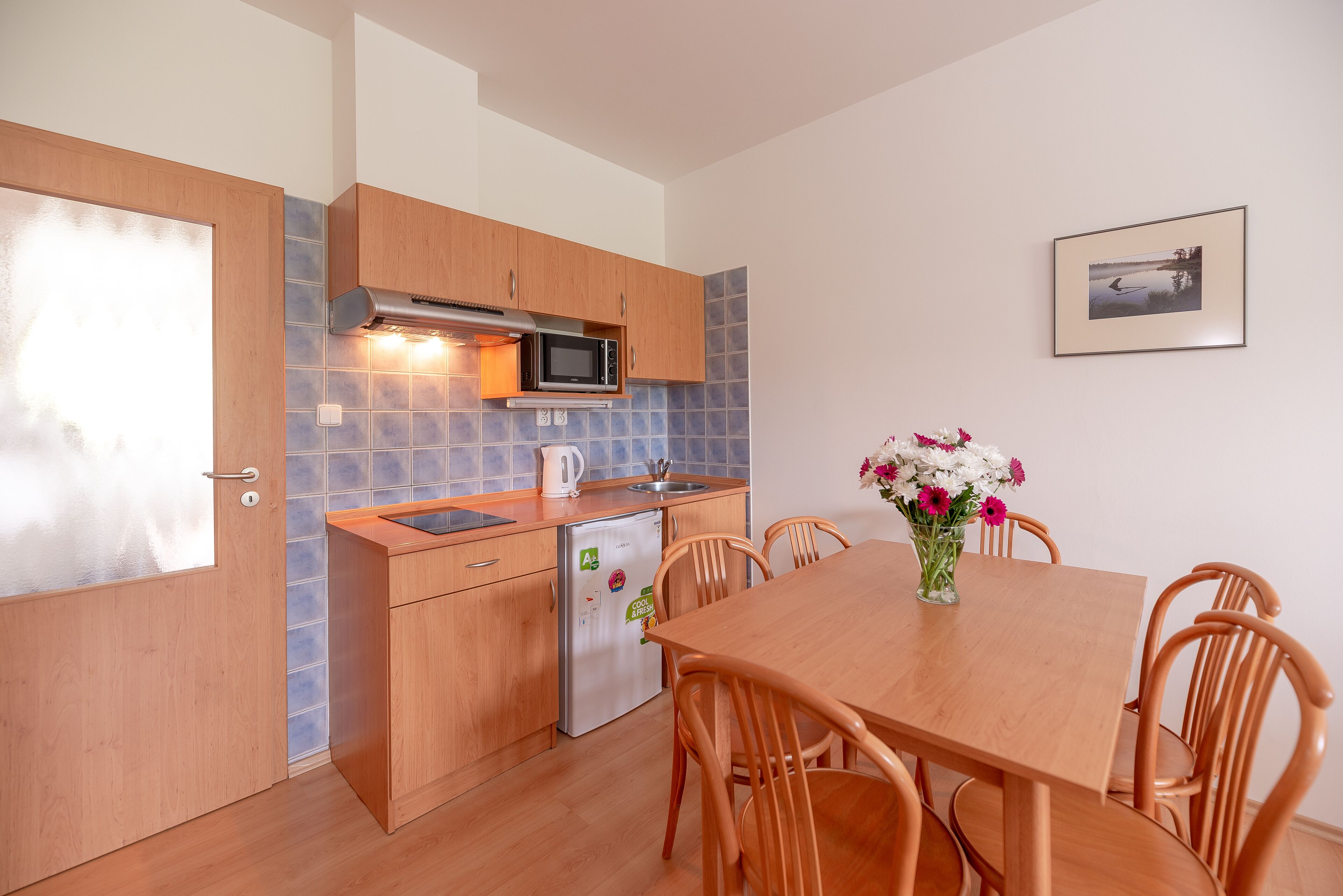 A kitchen with wooden cabinets, a microwave, a refrigerator, and a dining table with chairs.