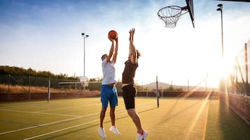 An outdoor basketball court with two players in motion, a clear sky, and distant mountains.